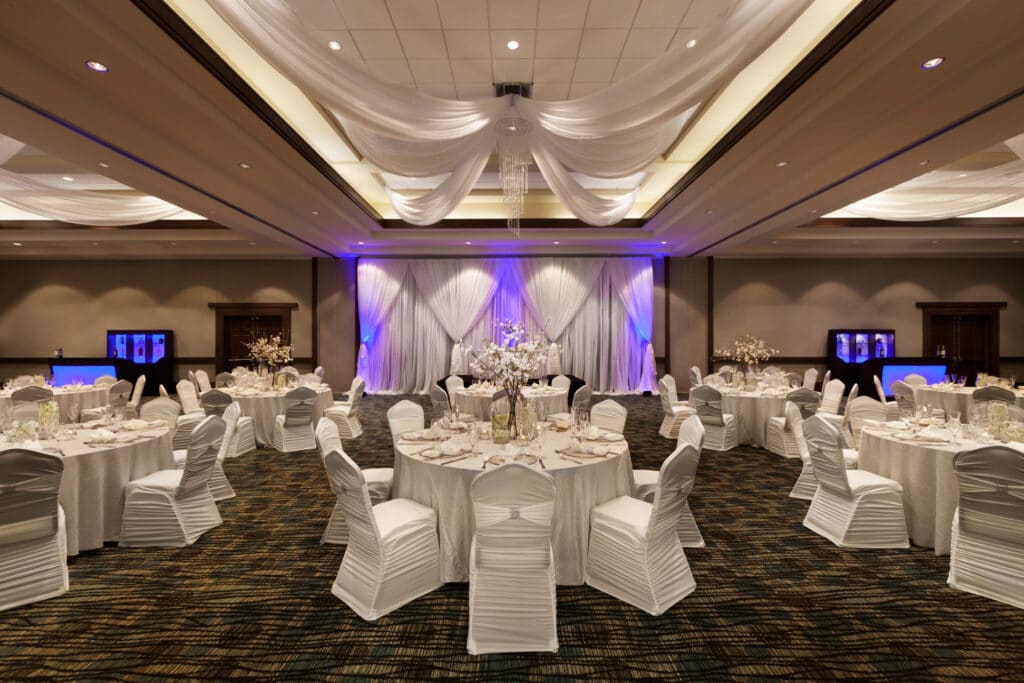 hotel ballroom set up for wedding reception with white tables and chairs and white drapery from ceiling